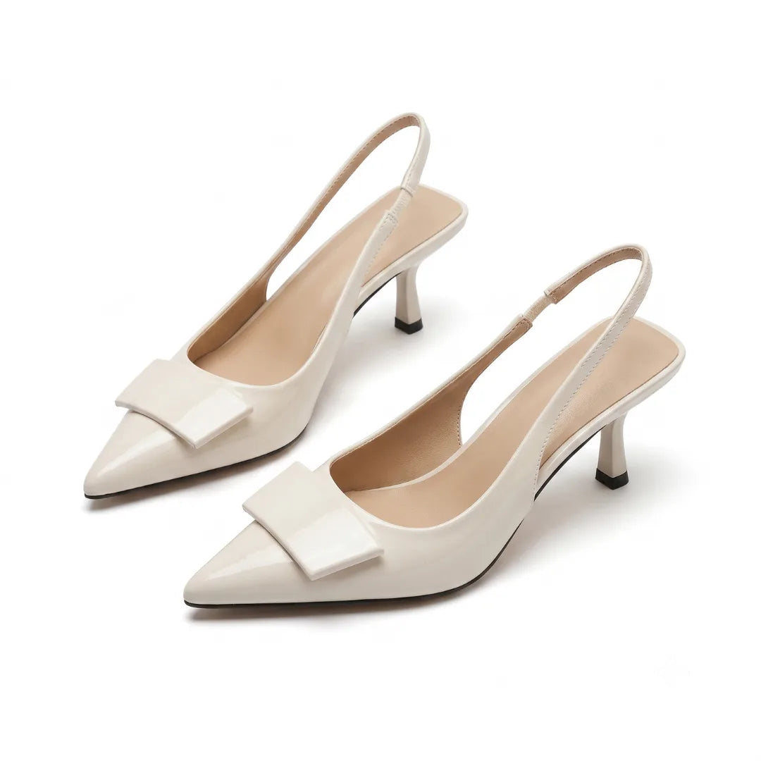 Angled pair shot of cream patent slingback pumps with pointed toe, buckle trim and slender kitten heel on a plain background
