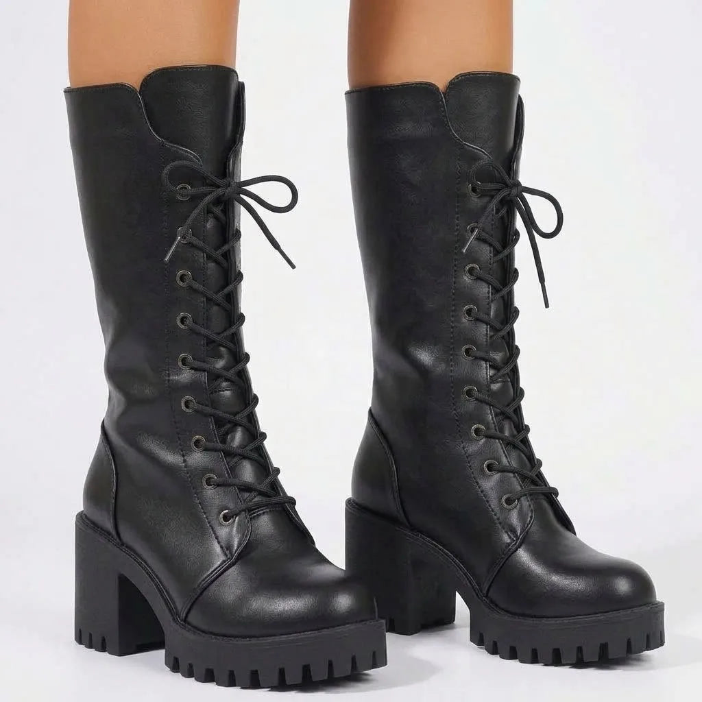 Front view of a model wearing black lace-up platform combat boots, laces tied in a bow at the ankle