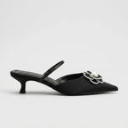 Studio side profile of a black satin mule with pointed toe, slim slingback strap and silver-outlined pearl flower embellishment