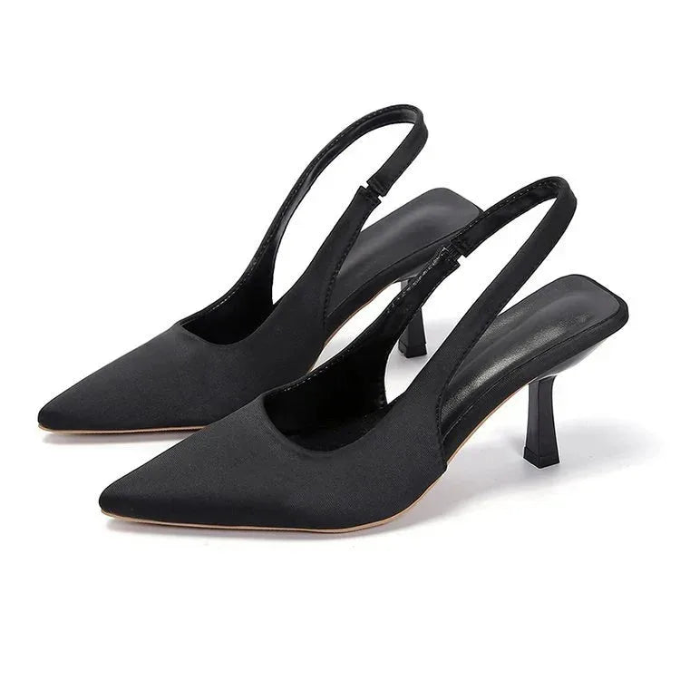 Angled view of black satin-finish slingback pumps with pointed toe and slender kitten heel