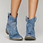 Close view of blue suede ankle boots with pointed toe, western-style stacked heel and burnished sole, worn on bare legs
