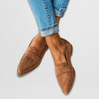 Tan suede pointed-toe loafers with penny strap detail worn on crossed ankles over rolled light denim