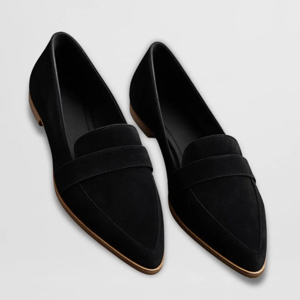 Pair of black suede pointed-toe loafers with penny strap, shown flat lay with tan leather soles visible