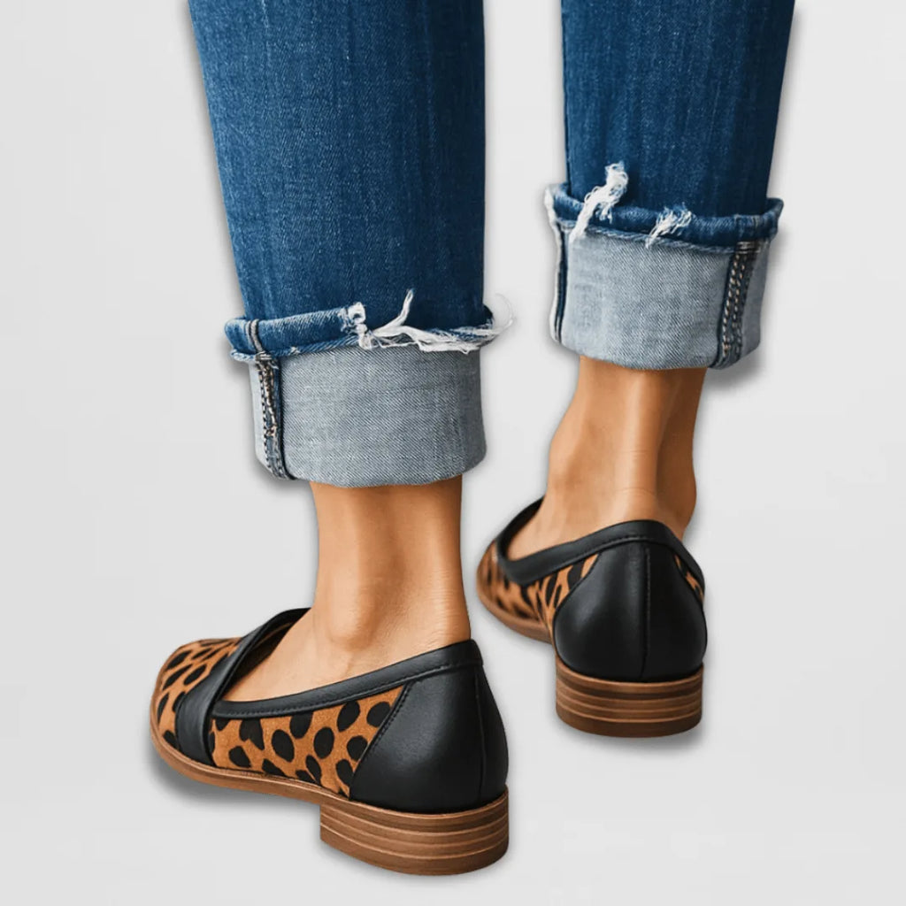 Back view of leopard-print loafers with black trim and stacked wooden heel, worn with frayed cuffed jeans