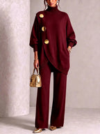 Woman wearing a burgundy polo neck tunic with gold disc buttons and matching wide-leg knit trousers, holding a gold handbag