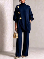 Navy knit tunic and trouser set photographed against a neutral studio backdrop with gold handbag detail