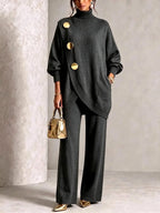 Front view of a charcoal grey asymmetric polo neck jumper with three gold buttons styled with matching wide-leg trousers
