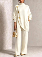 Cream knit polo neck tunic with diagonal gold-button placket and wide-leg trousers, shown with gold accessories