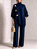 Navy blue polo neck jumper and trouser set with gold disc buttons, worn with a gold handbag and pointed heels