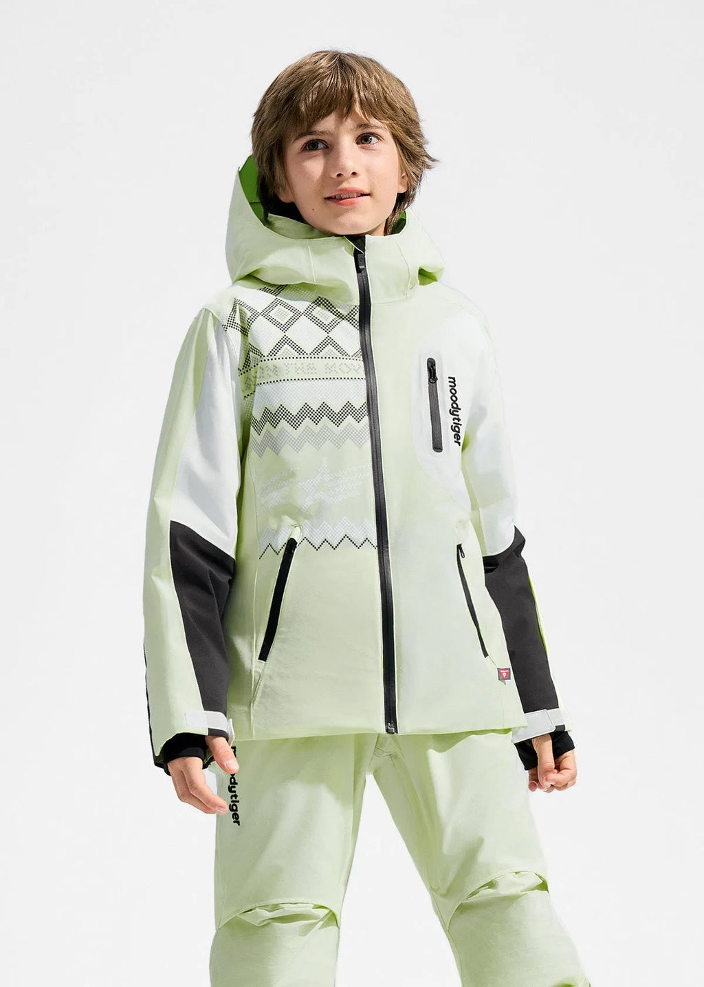 Boy wearing a pale green insulated ski jacket with hood up, colourblock white and black sleeves, standing against a plain backdrop