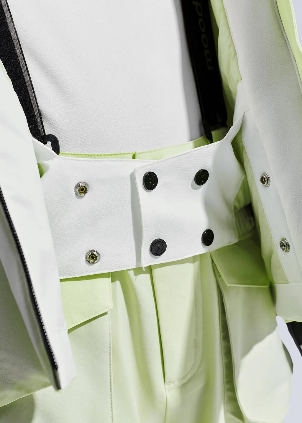 Close-up of the jacket's snap-button waist tab and interior powder skirt fastening in white and pale green