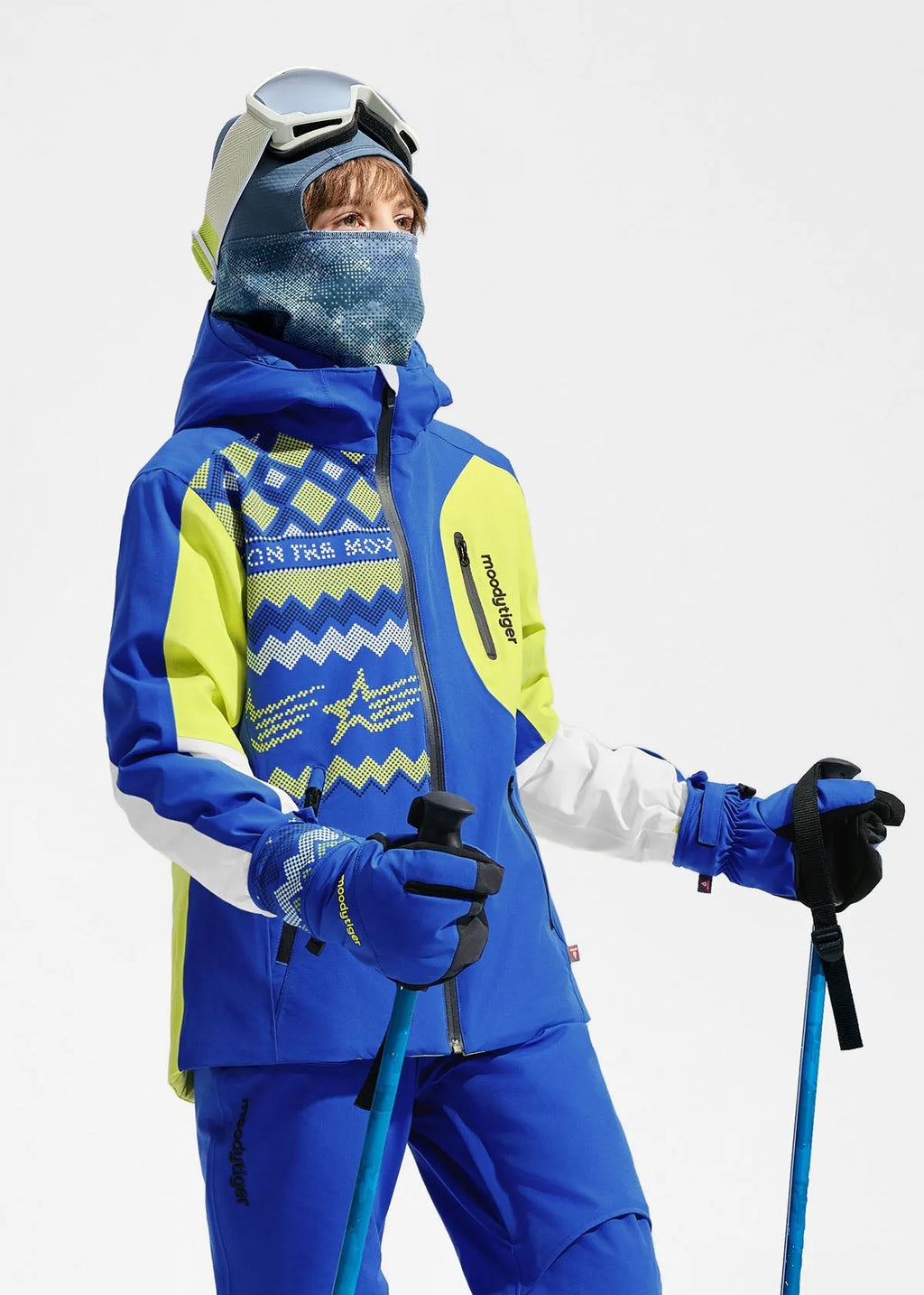 Girl wearing the ski jacket and trousers set in bright blue with lime green colourblock panels and a printed graphic