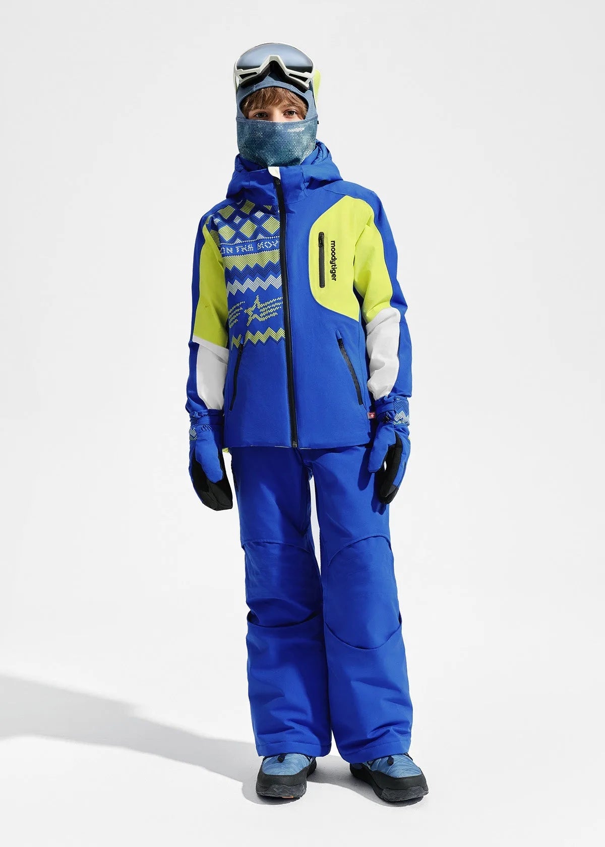 Front full-length view of boy in indigo blue ski jacket and matching salopette-style trousers, wearing goggles and a face gaiter