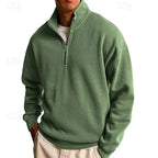 Front view of a sage green quarter-zip sweatshirt paired with cream trousers, hands in pockets