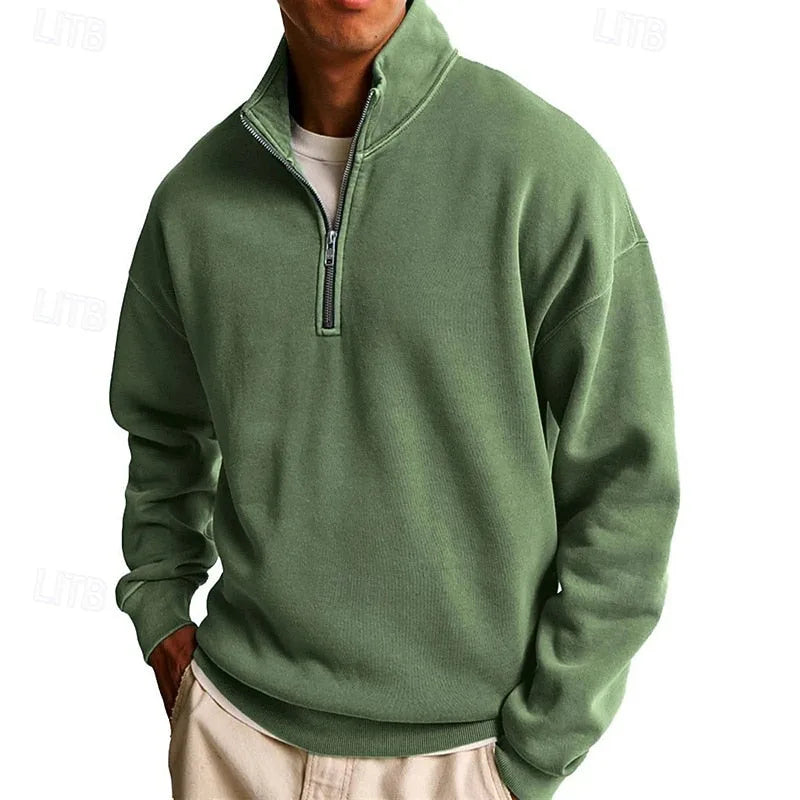 Front view of a sage green quarter-zip sweatshirt paired with cream trousers, hands in pockets