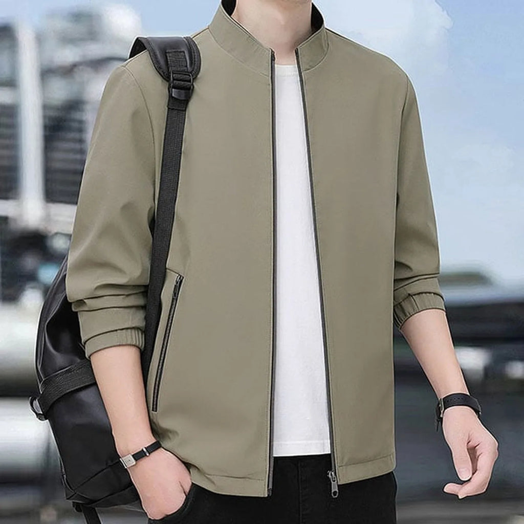 Man wearing the khaki jacket outdoors with a backpack strap across one shoulder