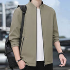 Man wearing the khaki jacket outdoors with a backpack strap across one shoulder