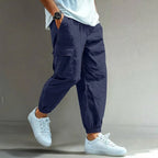 Side view of navy blue cotton cargo trousers with elastic waist, side pocket flap and elastic cuffs, worn with white trainers