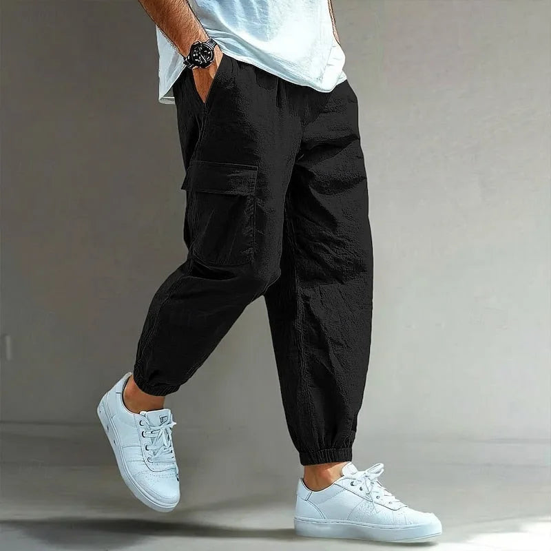 Black cargo trousers with elastic waist, side cargo pocket and elastic ankle cuffs, worn with white trainers