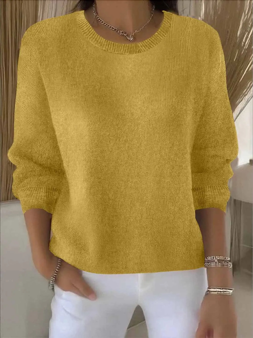 Close-up front view of mustard yellow knit jumper with ribbed round neckline worn with white trousers