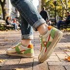 Side view of retro trainer worn walking, cream canvas upper with green suede panels and orange heel accent