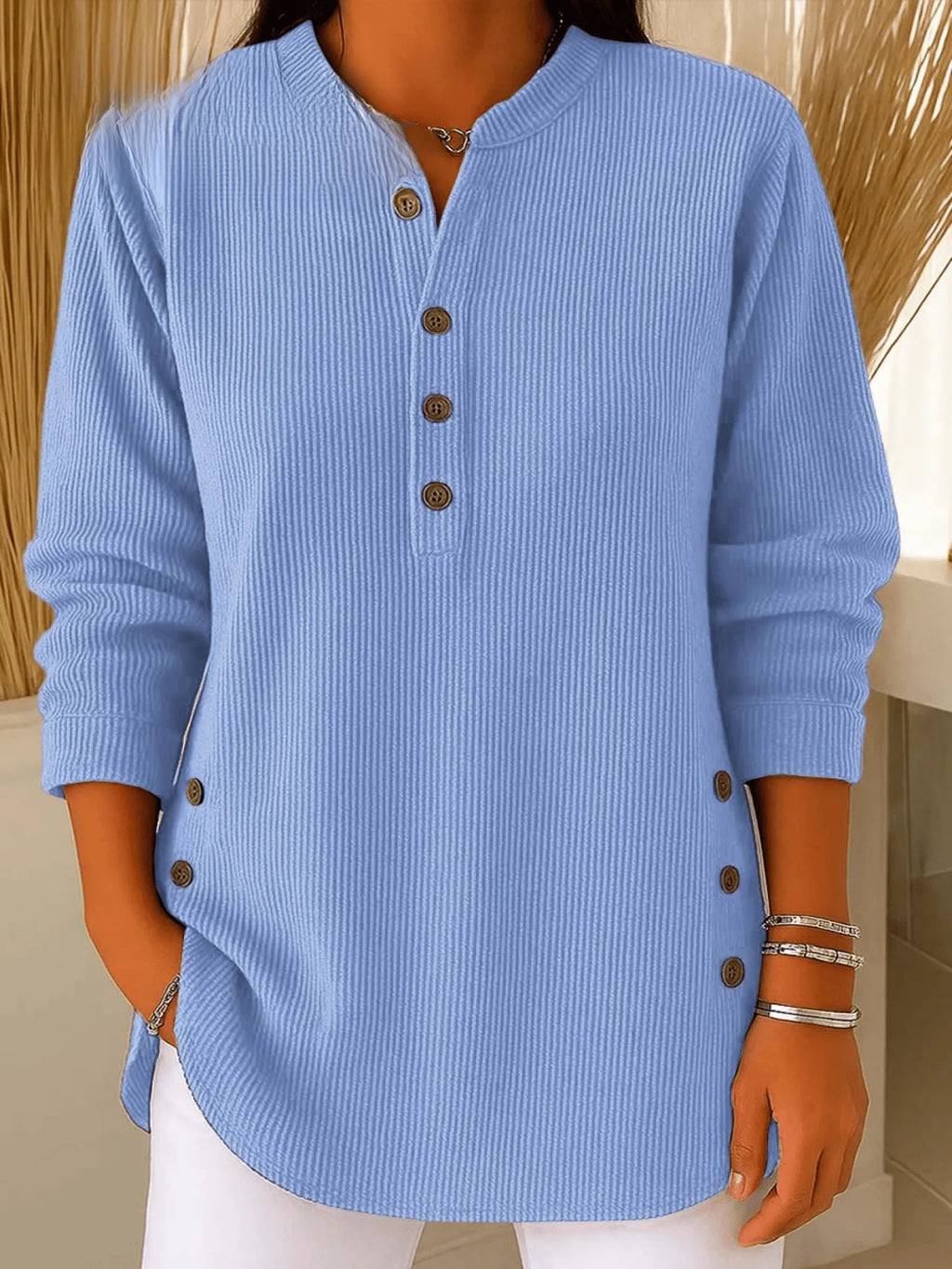 Close-up front view of a light blue ribbed tunic top with Henley neckline and brown button placket