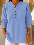 Close-up front view of a light blue ribbed tunic top with Henley neckline and brown button placket