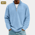 Man wearing a light blue ribbed quarter-zip jumper with silver zip, hands in pockets, front close-up view