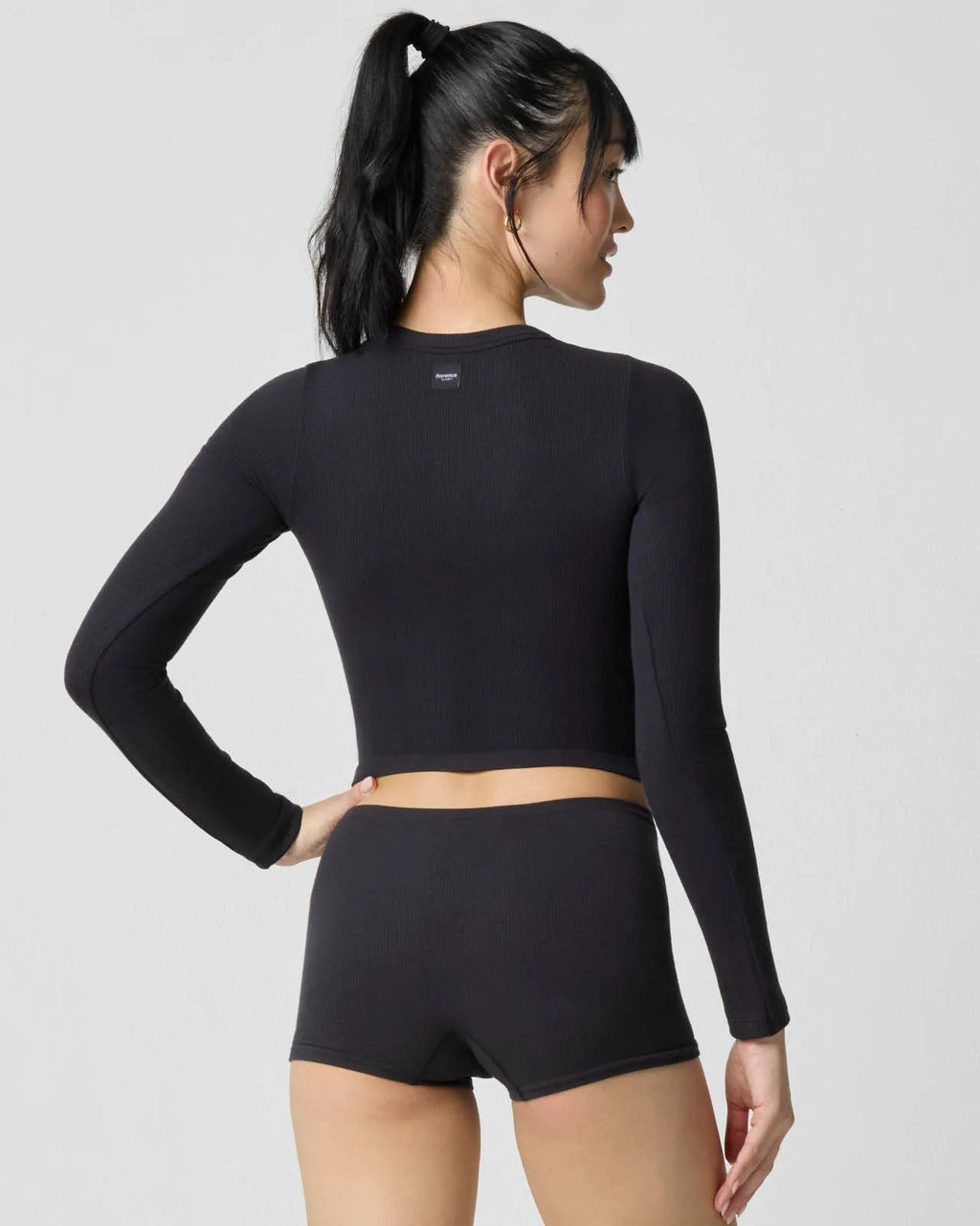 Back view of model wearing the black ribbed crop top and shorts, showing fitted raglan-style sleeve seams