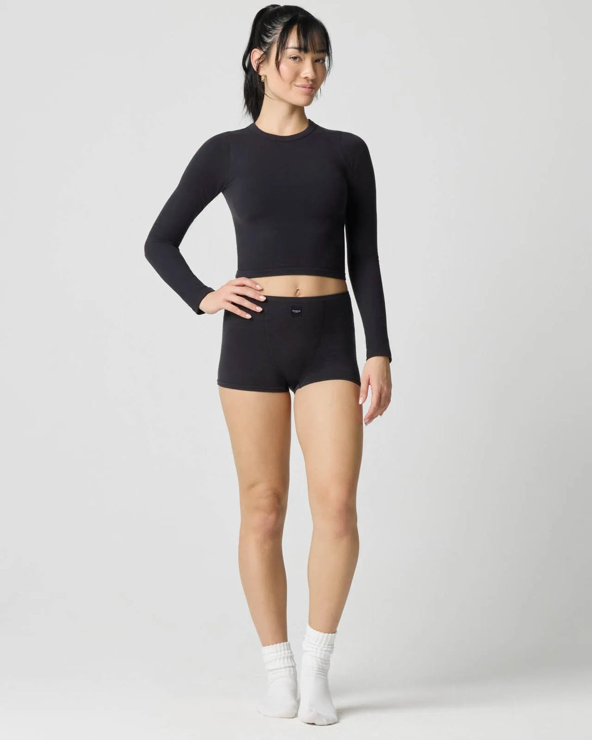 Full-length front view of model wearing the black ribbed long sleeve crop top with matching shorts and white socks