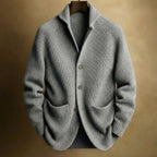Grey ribbed knit cardigan with notch collar and front patch pockets, hanging against a warm backdrop