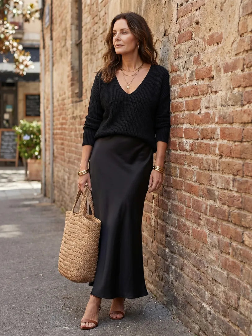 Full outfit view from a slight angle showing the jumper, satin skirt and straw tote together