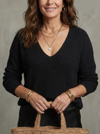 Close-up of the black ribbed V-neck jumper with layered gold necklaces and stacked gold bangles