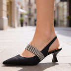 Close-up of black pointed-toe kitten heels with crystal strap worn on foot, city backdrop