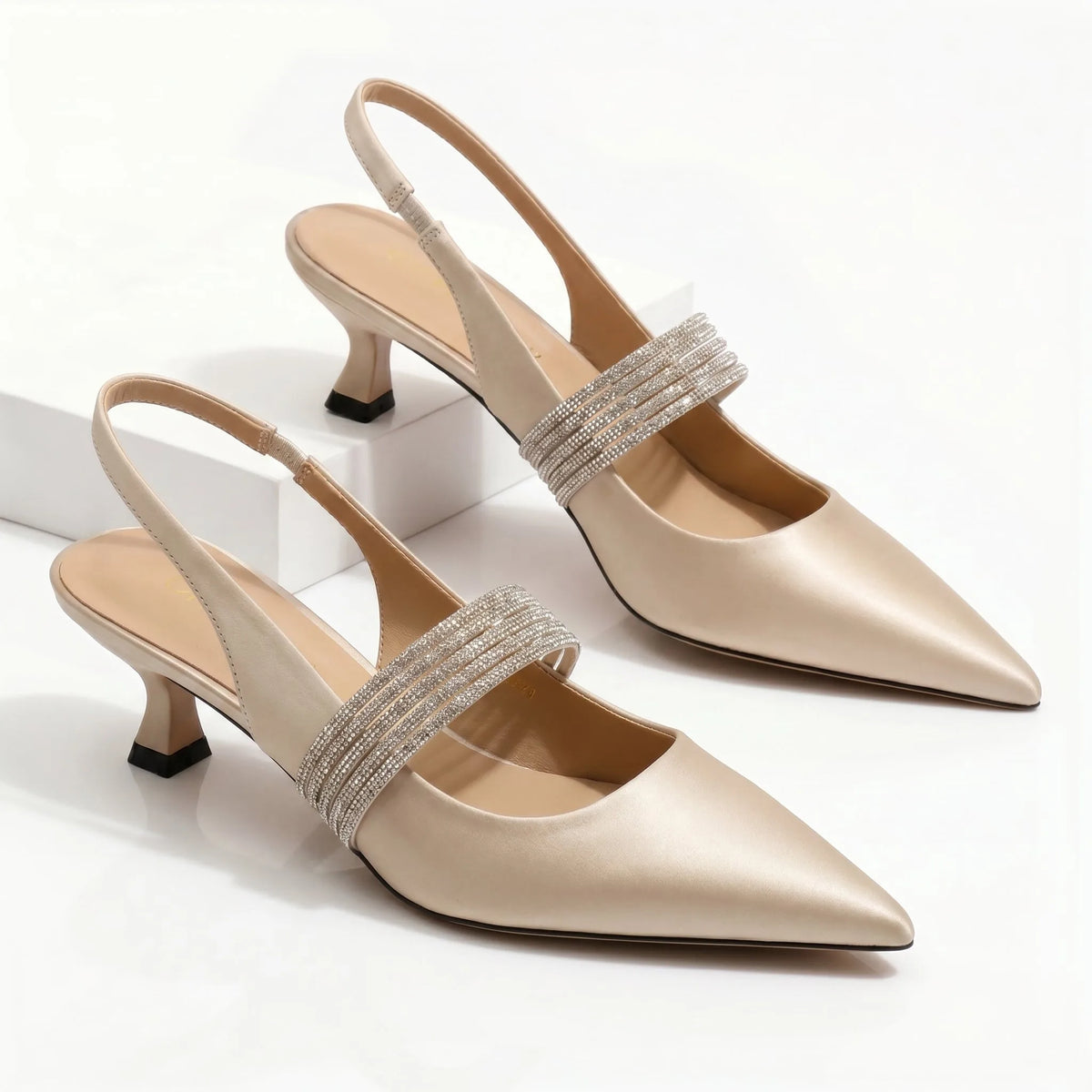 Pair of champagne satin pointed-toe kitten heels shown together with crystal ankle strap detail