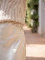 Close-up of the ribbed jumper hem resting over the ivory satin skirt waistband, showing knit texture against smooth fabric