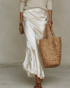 Close-up of the ivory satin skirt draped with soft folds, worn under a cream jumper, paired with brown leather sandals