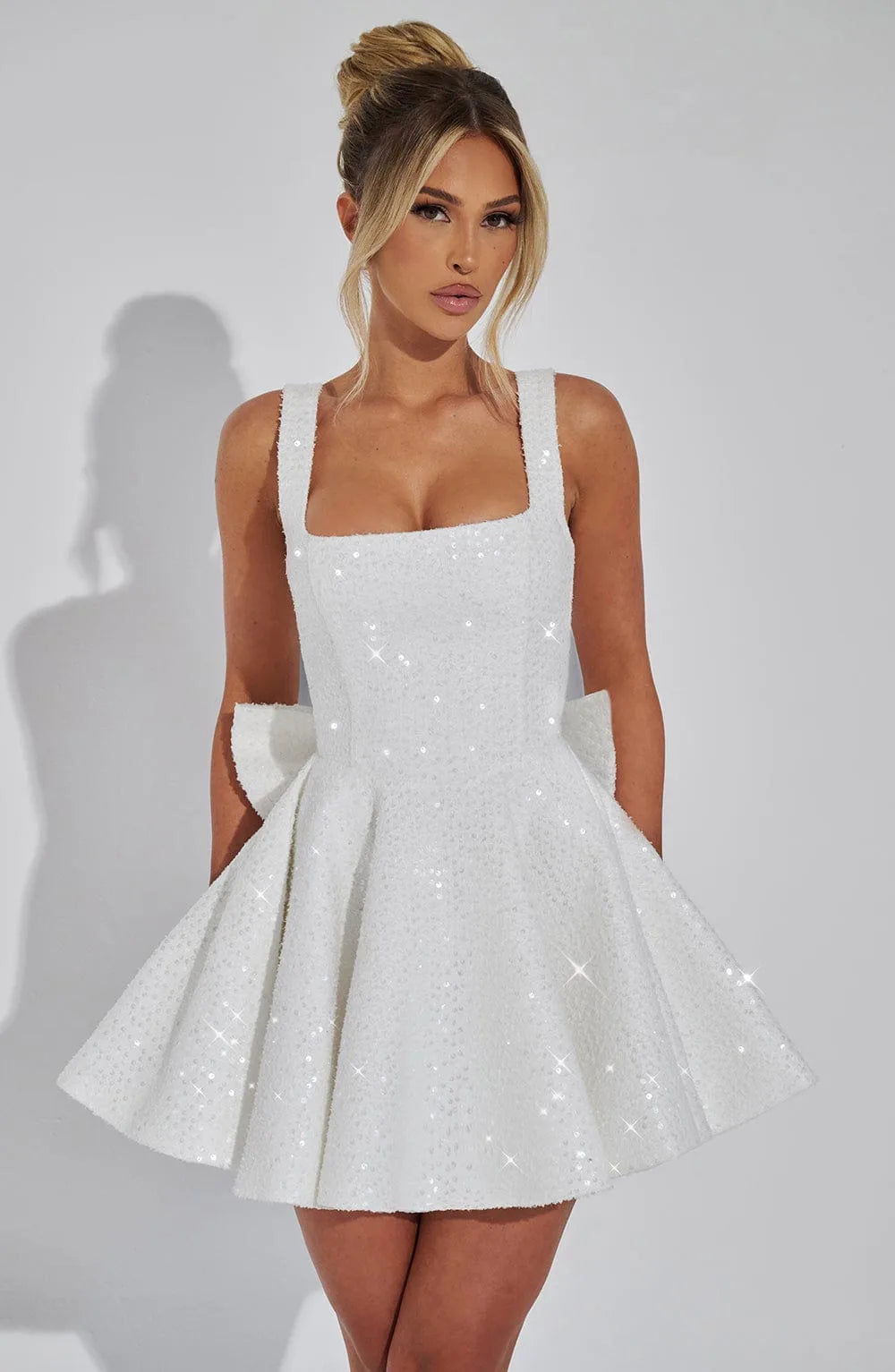Front view of a woman wearing an ivory sequin fit-and-flare mini dress with a square neckline and full skater skirt