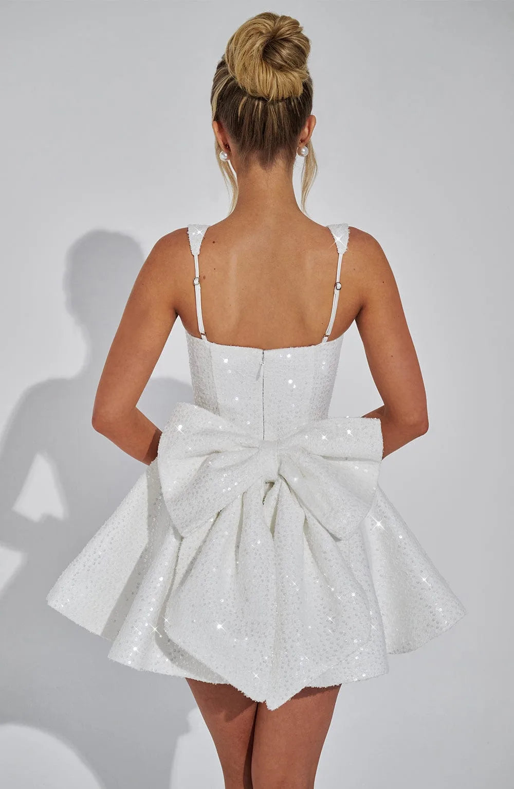 Back view showing the ivory sequin mini dress with a large oversized bow detail covering the open back