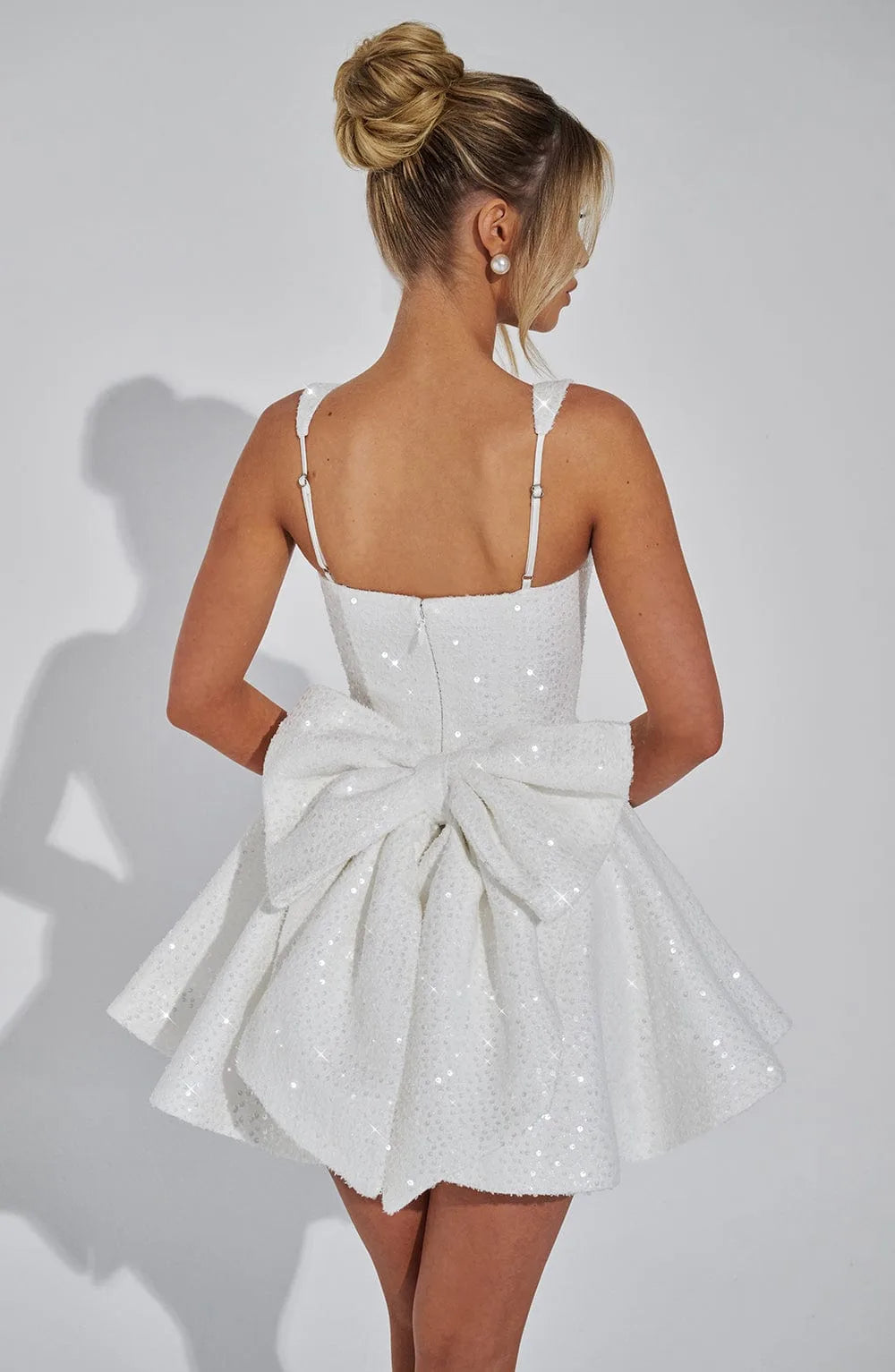 Three-quarter view of the ivory sequin mini dress highlighting the square neckline and voluminous pleated skirt