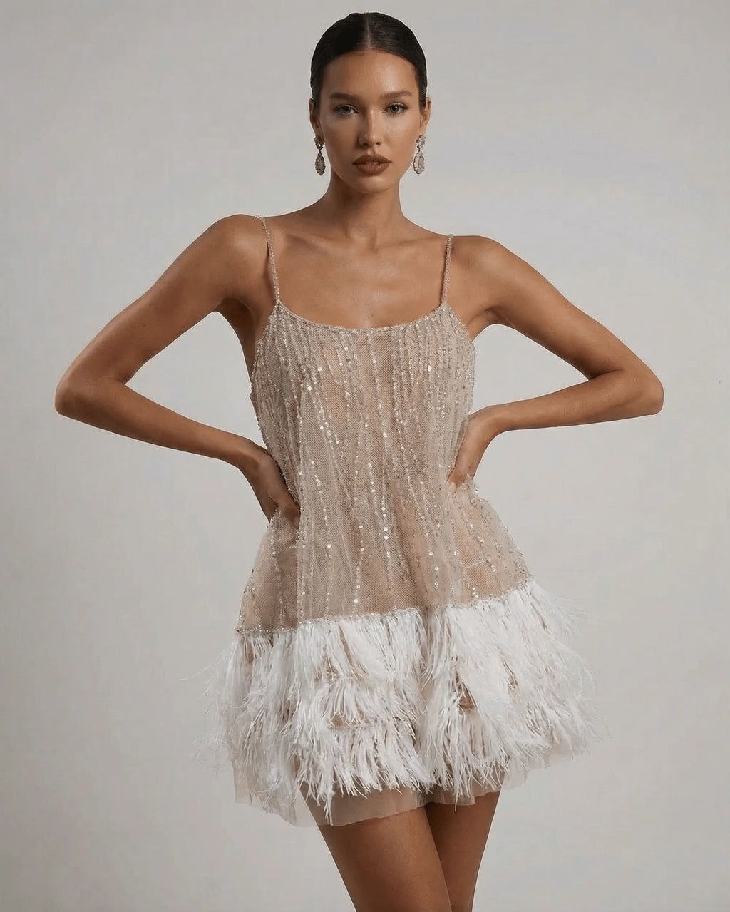 Front view of beige sequin mini dress with scoop neckline, spaghetti straps and white ostrich feather hem