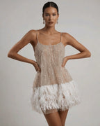 Front view of beige sequin mini dress with scoop neckline, spaghetti straps and white ostrich feather hem