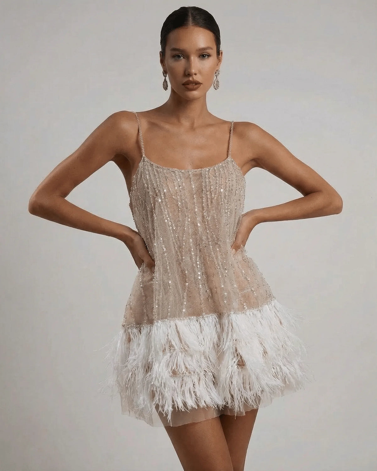 Front view of beige sequin mini dress with scoop neckline, spaghetti straps and white ostrich feather hem