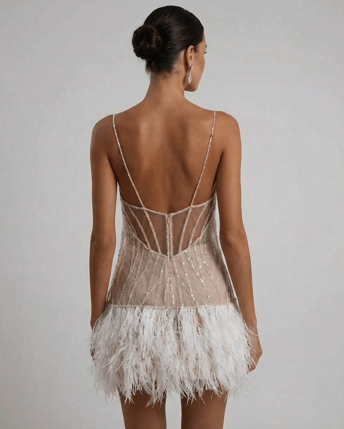 Back view showing sheer corset-style panelling, geometric straps and low back on the sequin feather mini dress
