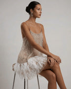 Seated side view showing the drop-waist cut, sequin bodice and fluffy white feather trim