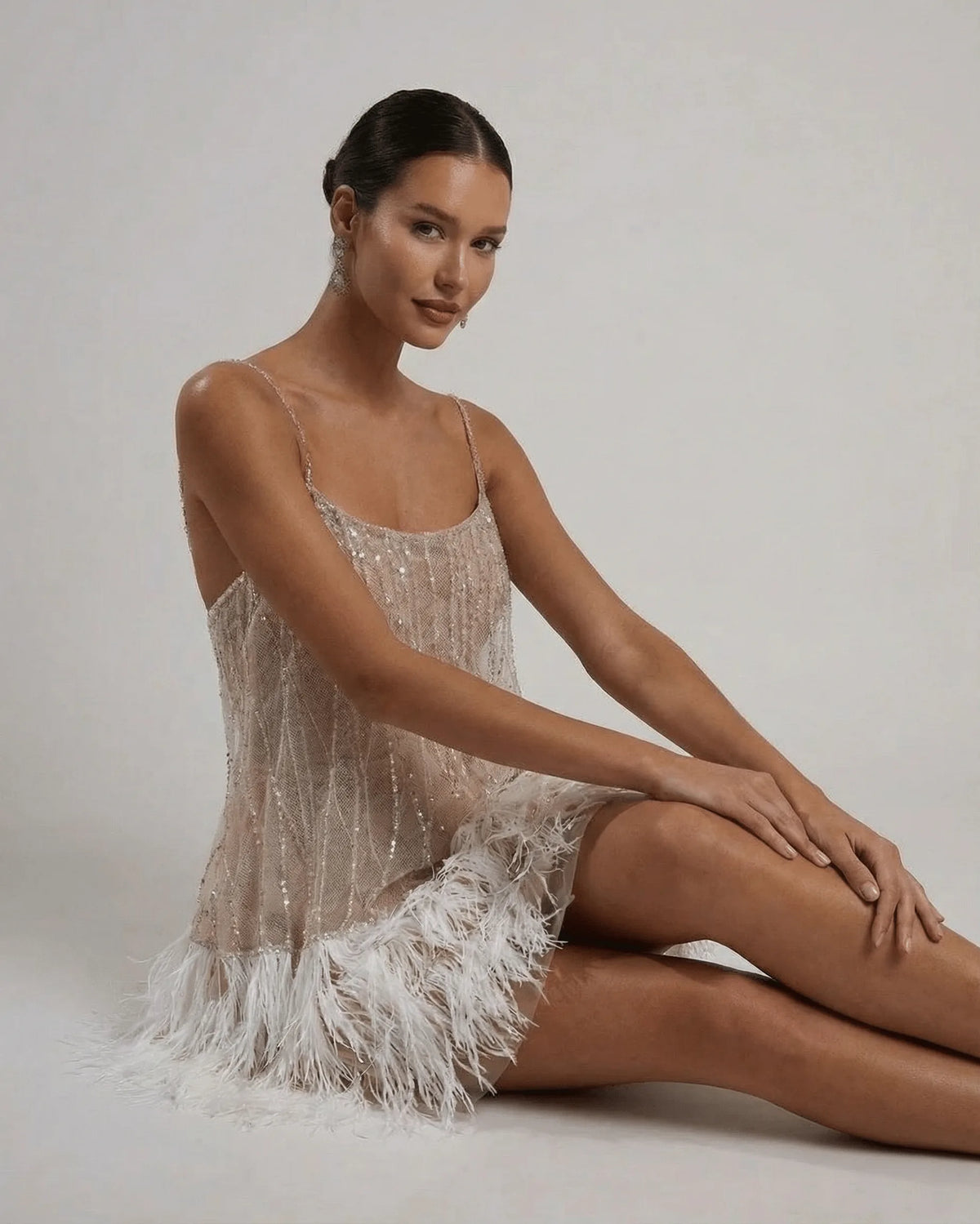 Seated close-up showing sequin detailing on the bodice and texture of the ostrich feather hemline