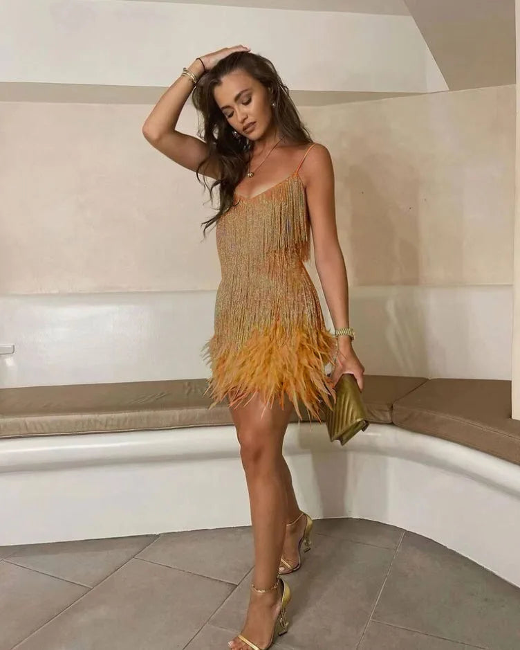 Woman posing in an orange ombre sequin fringe mini dress with feather hem and matching gold heeled sandals
