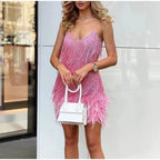 Woman holding a white handbag while wearing a pink ombre sequin fringe mini dress with a feathered skirt hem
