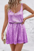 Front view of a purple sequin mini dress cinched at the waist with a belt, paired with a clutch bag