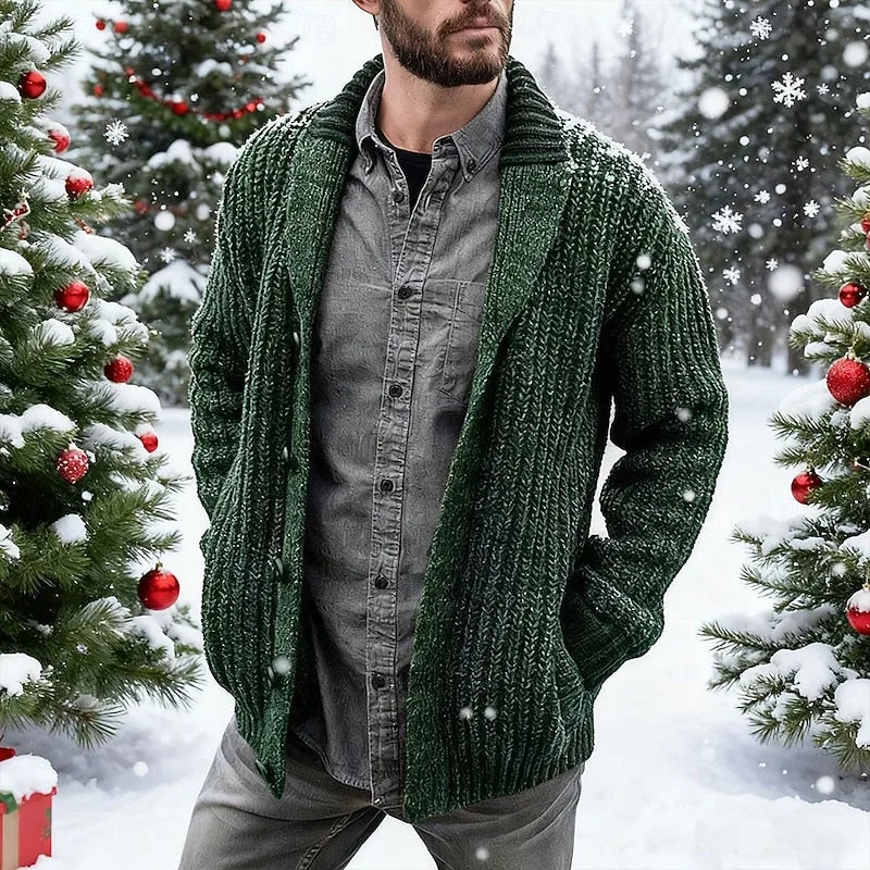 Man wearing a green ribbed knit shawl collar cardigan open over a grey button-down shirt, standing among snowy Christmas trees